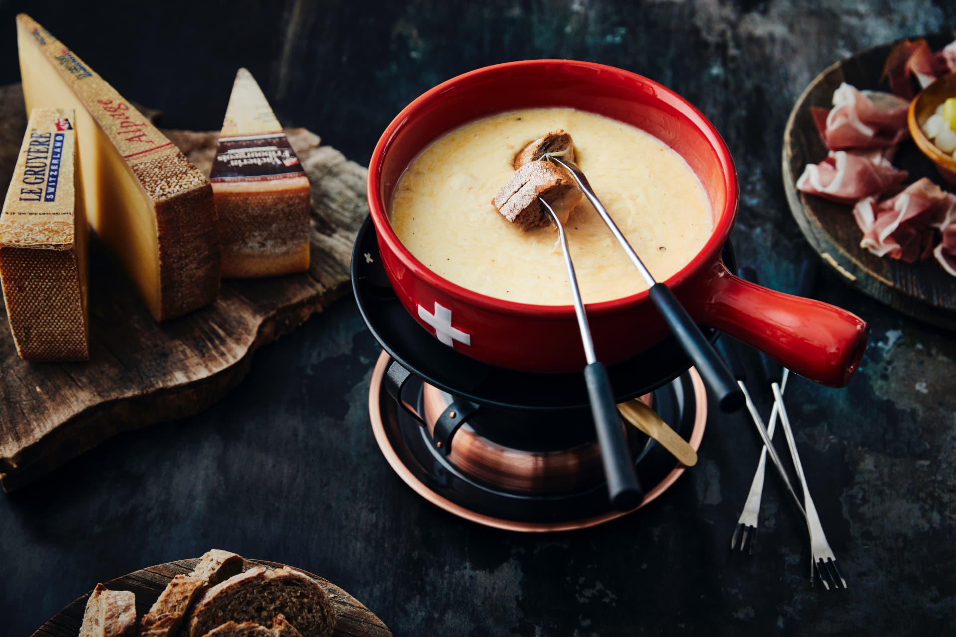 Fondue au fromage servi dans un caquelon rouge à croix suisse, avec Le Gruyère AOP et Vacherin Fribourgeois
